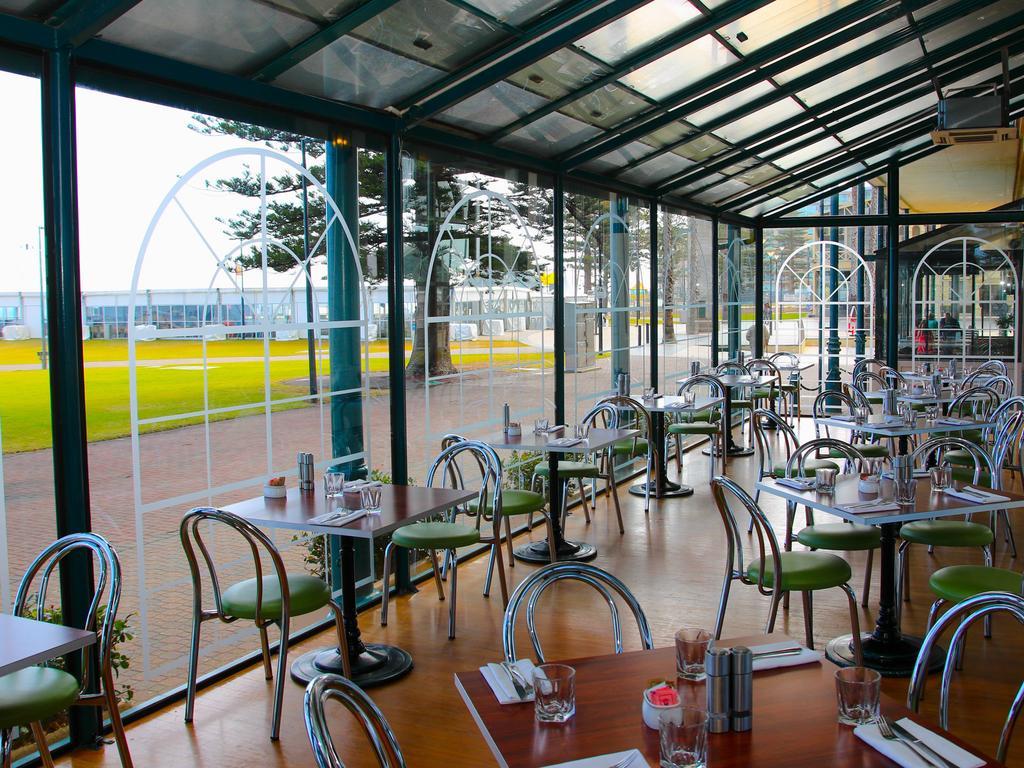 Отель Stamford Grand Adelaide Гленелг Экстерьер фото The photo shows the interior of a restaurant with a modern design. The space features several tables with green chairs, arranged in a way that allows for ample seating. Large glass windows provide a view of the outside, creating a bright and open atm